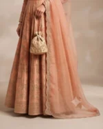 Detailed close-up of the pleated skirt hem of a peach Anarkali suit, a sheer embroidered dupatta border, and a matching gold embroidered potli bag accessory