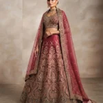 Full-length studio portrait of a model wearing a blush pink silk lehenga with intricate floral gold embroidery and full sleeves